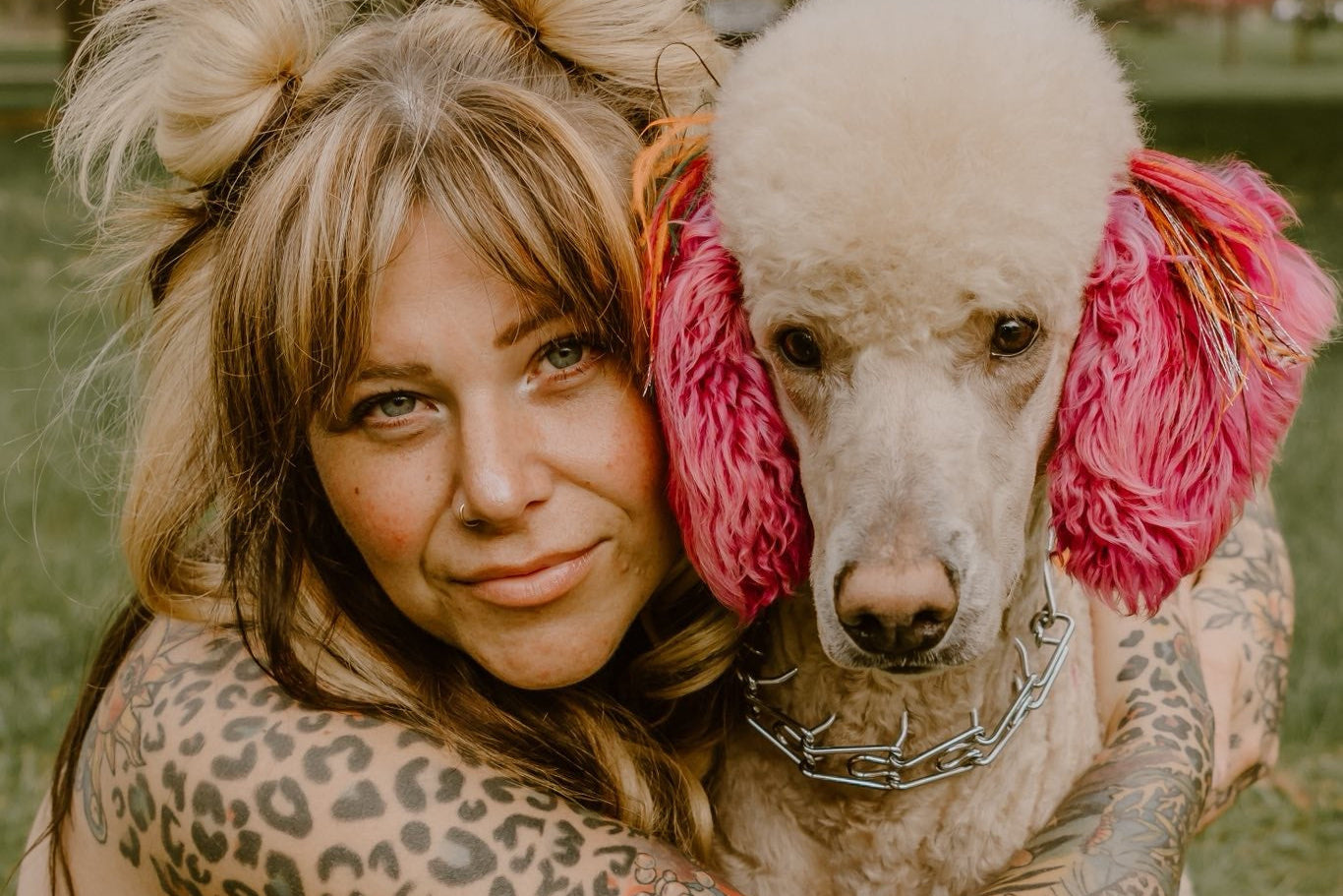 Woman with tattoos hugging a poodle with pink bows outdoors